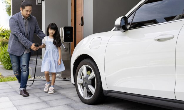 Un père et une fille progressistes chargeant une voiture électrique à partir d'une station de charge à domicile
