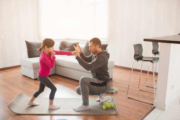 Le père et la fille s'entraînent à la maison. Séance d'entraînement dans l'appartement. Sports à la maison. Père enseigne à garder un coup de poing. Boxe ensemble. Stage de boxe à domicile