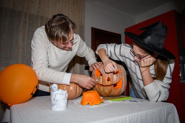 Photo père et fille sculptant des citrouilles jack o lanternes à la fête d'halloween à la fête de la cuisine maison de vacances d'automne traditionnelle