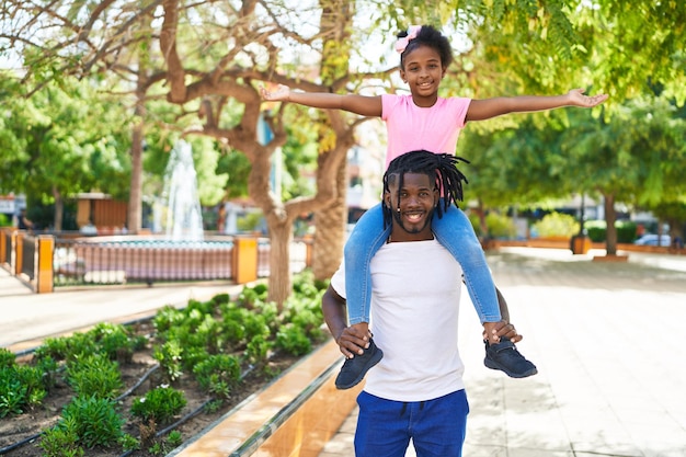 Père et fille souriant confiant tenant une fille sur les épaules au parc