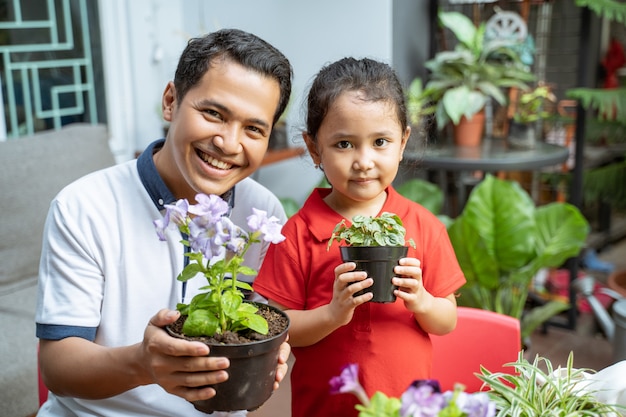 Père et fille tiennent des plantes en pot et souriant à la caméra