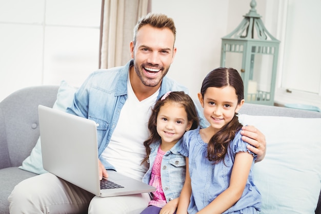 Père et filles avec ordinateur portable assis sur un canapé