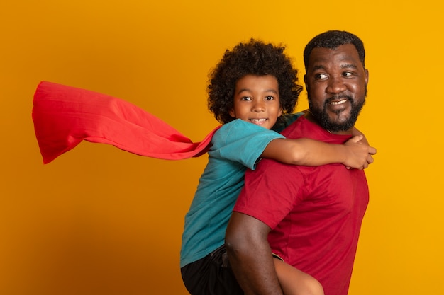 Père et fils africains jouant Superhero à la journée. Gens s'amusant mur jaune. Concept de famille sympathique.