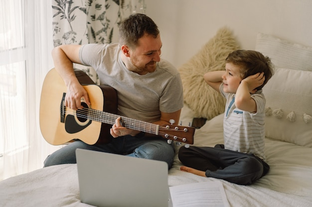 Père et fils apprennent à jouer de la guitare acoustique dans une leçon en ligne.