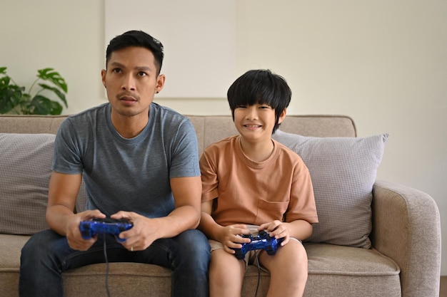 Un père et un fils asiatiques excités avec des joysticks jouent ensemble à des jeux vidéo à la maison