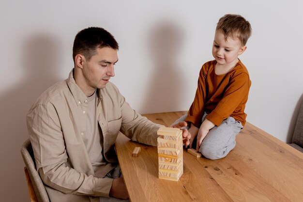 Père et fils assis ensemble à la maison et jouant avec des blocs de bois Jeu Jenga Petit garçon et son père passent du temps ensemble Temps en famille Activité de loisirs à l'intérieur