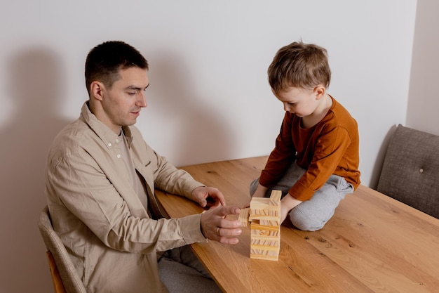 Père et fils assis ensemble à la maison et jouant avec des blocs de bois Jeu Jenga Petit garçon et son père passent du temps ensemble Temps en famille Activité de loisirs à l'intérieur