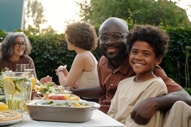 Père et fils assis à table avec de la nourriture faite maison et regardant la caméra