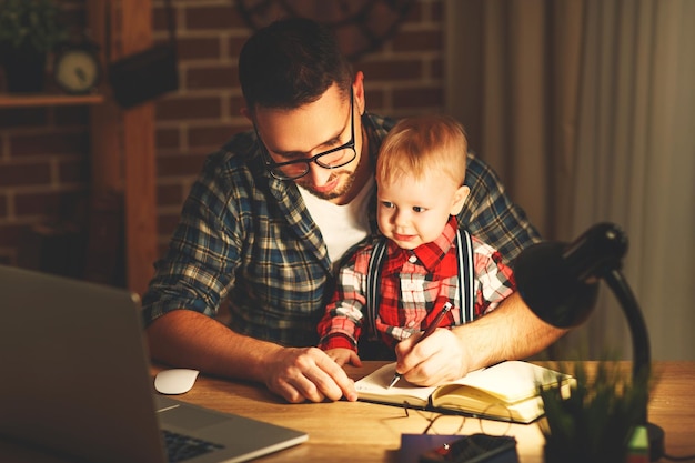 Père et fils bébé travaillent à la maison à l'ordinateur dans l'obscurité