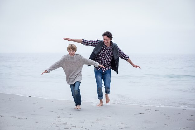 Père et fils courir sur la plage avec les bras tendus