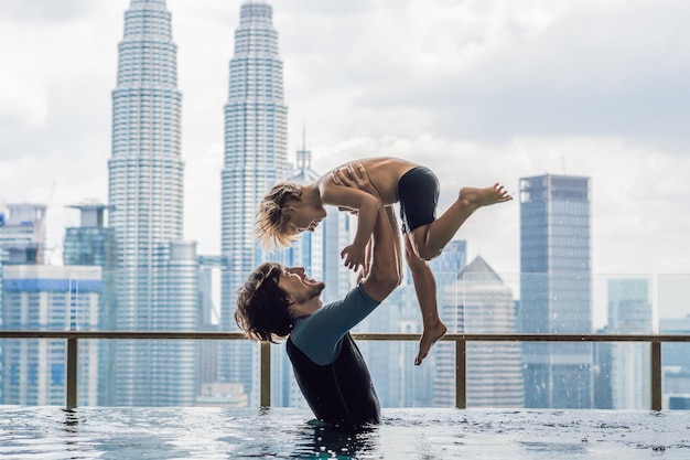 Père et fils dans une piscine extérieure avec vue sur la ville dans le ciel bleu