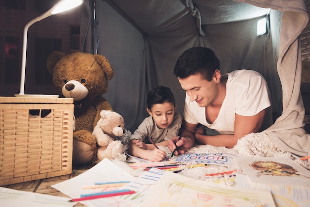 Père et fils dessinent avec des crayons de couleur sur papier.