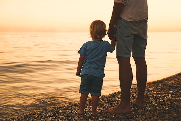 Père et fils dos silhouettes marchant au bord de la mer Homme et enfant garçon jouant ensemble à l'extérieur sur une plage de la mer Famille aimante et vacances d'été