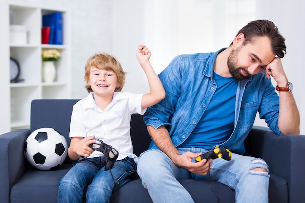 Père et fils drôles avec des manettes jouant au jeu vidéo à la maison