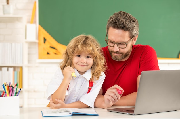 Père et fils étudient en classe avec ordinateur portable, école.