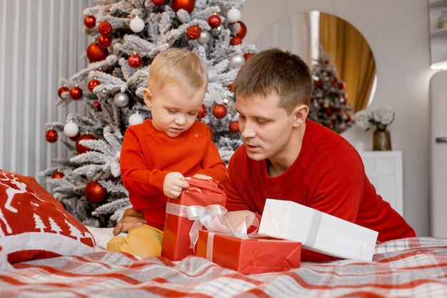 Père et fils avec des expressions faciales sérieuses ouvrant des cadeaux de Noël assis près de l'arbre du Nouvel An