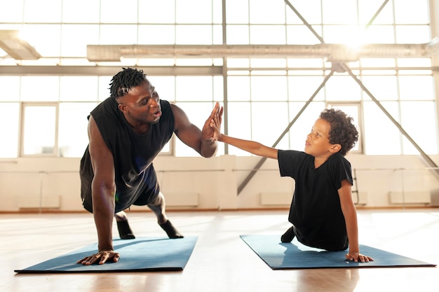 père et fils font du sport dans la salle de sport et donnent un high five à un garçon afro-américain avec papa faisant des pompes