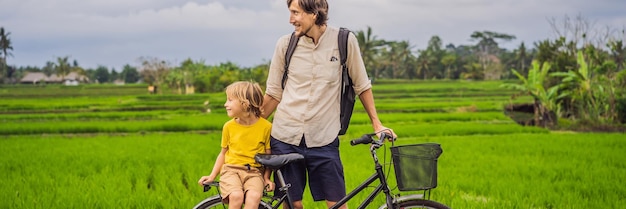 Père et fils font du vélo sur une rizière à ubud bali voyagent à bali avec bannière de concept pour enfants