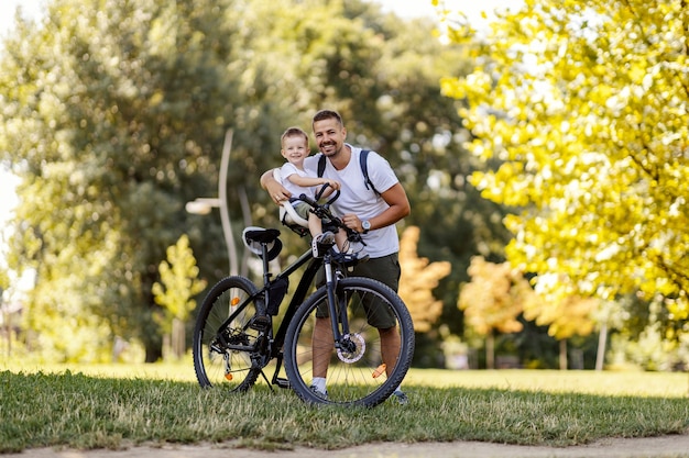 Père et fils font du vélo. Le tout-petit est assis dans le panier du vélo pendant que son père le tient pendant qu'il se repose après avoir fait du vélo à travers la forêt. Journée d'été ensoleillée en famille