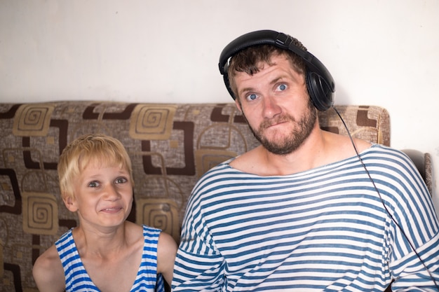 Photo père et fils en gilet écoutent de la musique au casque et s'amusent. émotions de surprise et de joie.