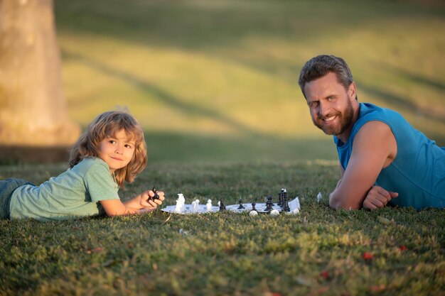 Père et fils jouant aux échecs allongé sur l'herbe au parc pelouse fête des pères amour famille parentalité enfant