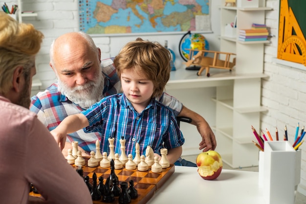 Père et fils jouant aux échecs petit-fils souriant heureux garçon avec papa et grand-père apprenant ensemble happ