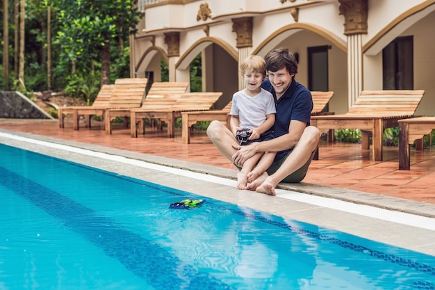 Père et fils jouant avec un bateau télécommandé dans la piscine