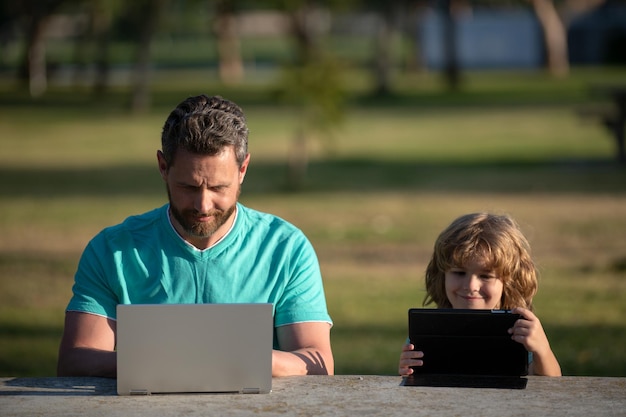 Père et fils jouant ou étudiant avec un ordinateur portable dans le parc enfant avec papa apprenant le blogging