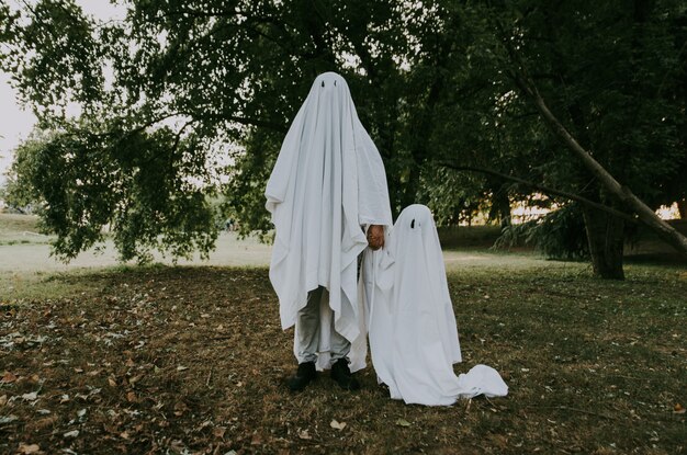 Père et fils jouant des fantômes avec des draps blancs dans le jardin, photos conceptuelles sur les vacances d'Halloween