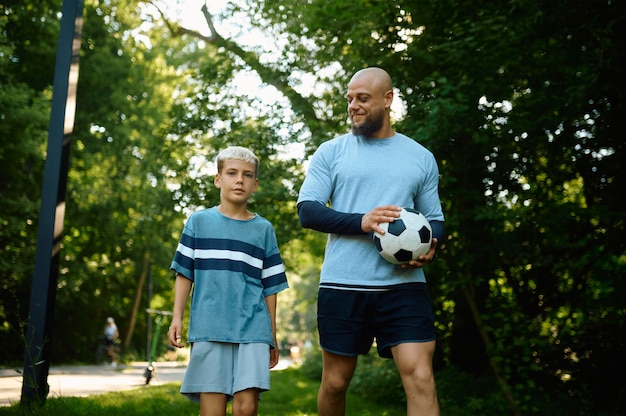 Père et fils jouent au football par une journée ensoleillée à l'extérieur. La famille mène un mode de vie sain, entraînement physique matinal dans le parc d'été