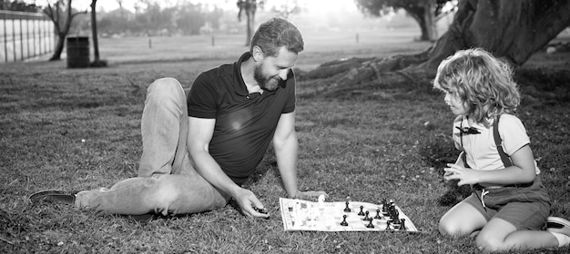 Père et fils jouent aux échecs sur l'herbe dans les échecs du parc d'été