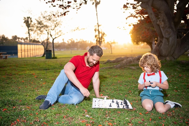 Père et fils jouent aux échecs sur l'herbe dans le parc d'été, l'enfance.