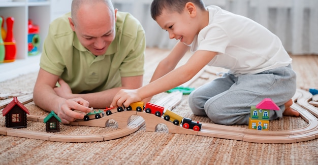 père et fils jouent sur un chemin de fer en bois jouet dans la salle de jeux.