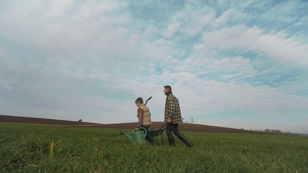 Le père et le fils marchant dans le champ avec une brouette