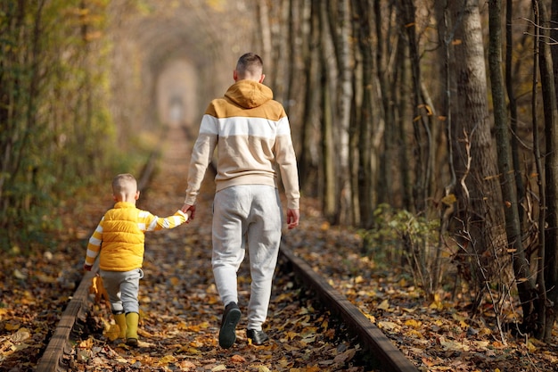 Père et fils marchent sur le chemin de fer en voyageant La famille passe du temps ensemble en vacances père et fils passent du temps ensemble en automne