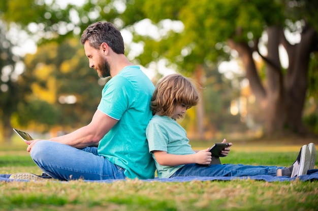 Père et fils avec ordinateur portable dans le parc papa enseigne à l'enfant l'utilisation de la technologie moderne l'apprentissage à distance lesso