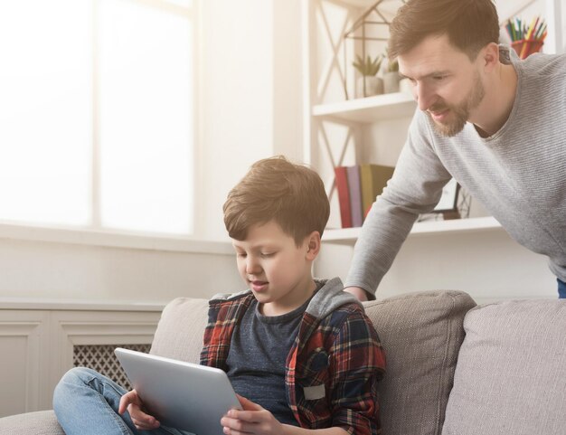 Père et fils passent du temps ensemble et utilisent une tablette numérique sur un canapé à la maison