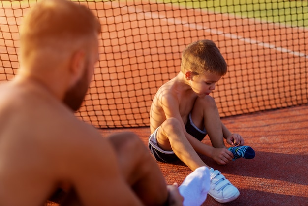 Père et fils prennent leurs chaussettes avant de s'entraîner au tennis par une chaude journée d'été.