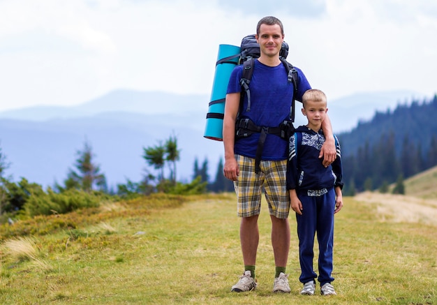 Père et fils avec des sacs à dos de randonnée ensemble dans les pittoresques montagnes vertes d'été. Papa et enfant debout appréciant la vue sur la montagne paysage. Mode de vie actif, relations familiales, concept d'activité de week-end.