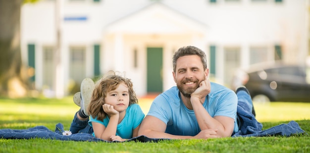 Père et fils sympathiques pour la fête des pères s'amusant dans le parc valeur familiale enfance et parentalité parent se détendre avec petit enfant garçon sur l'herbe papa avec enfant le jour d'été parentalité et paternité