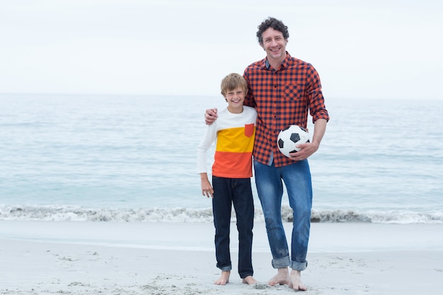 Père et fils tenant un ballon de foot au bord de la mer