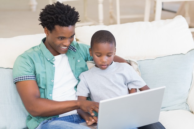 Père et fils utilisant un ordinateur portable sur le canapé