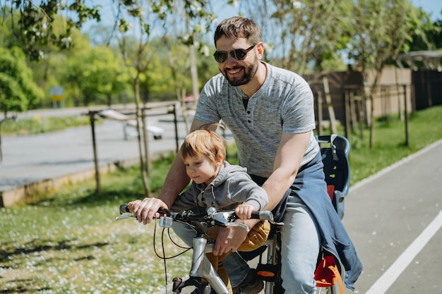 Père et fils à vélo ensemble sur un seul vélo le long de la piste cyclable. Notion de fête des pères. Image avec mise au point sélective. photo de haute qualité