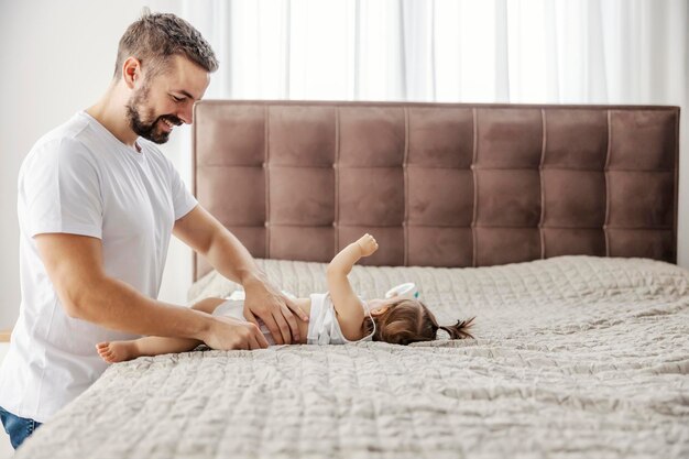 Un père heureux change de couche pendant que la petite fille joue et se retourne