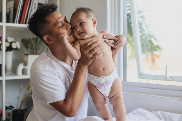 Un père heureux embrasse d'adorables joues de bébé tout en jouant à la maison