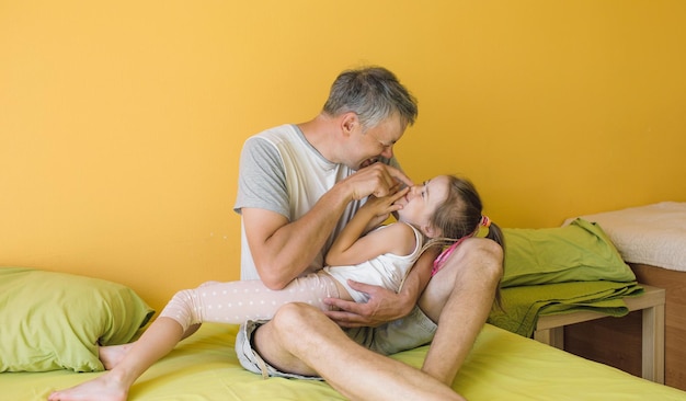 Un père heureux joue au lit avec sa petite fille. plaisir et joie de vacances communes