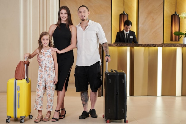 Un père heureux, une mère et une fille préadolescente avec des valises dans le hall de l'hôtel.