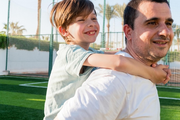 Photo un père heureux porte son fils sur le dos sur le terrain de sport