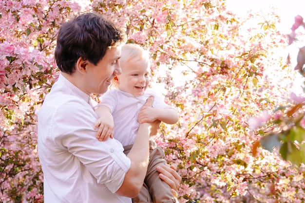 père heureux avec son fils sur le fond d'un arbre en fleurs dans l'arrière-cour de la maison