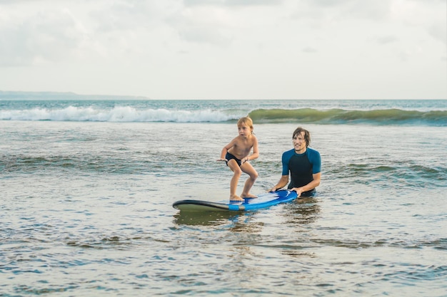 Père ou instructeur apprenant à son fils de 4 ans à surfer en mer en vacances ou en vacances. Concept de voyage et de sport avec enfants. Cours de surf pour les enfants